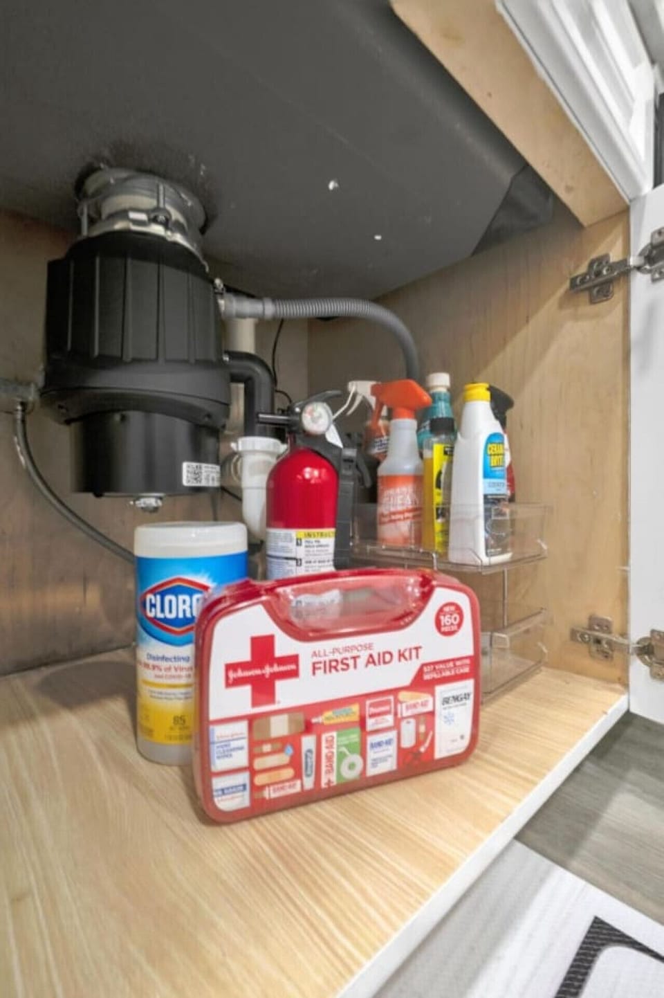Organized under-sink storage with cleaning supplies, a first aid kit, and a fire extinguisher.