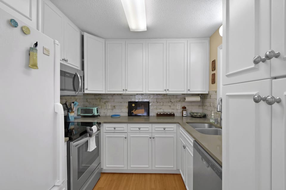 Kitchen and Refrigerator - Kitchen angle showing refrigerator, range, microwave, cabinetry, and tile backsplash.
