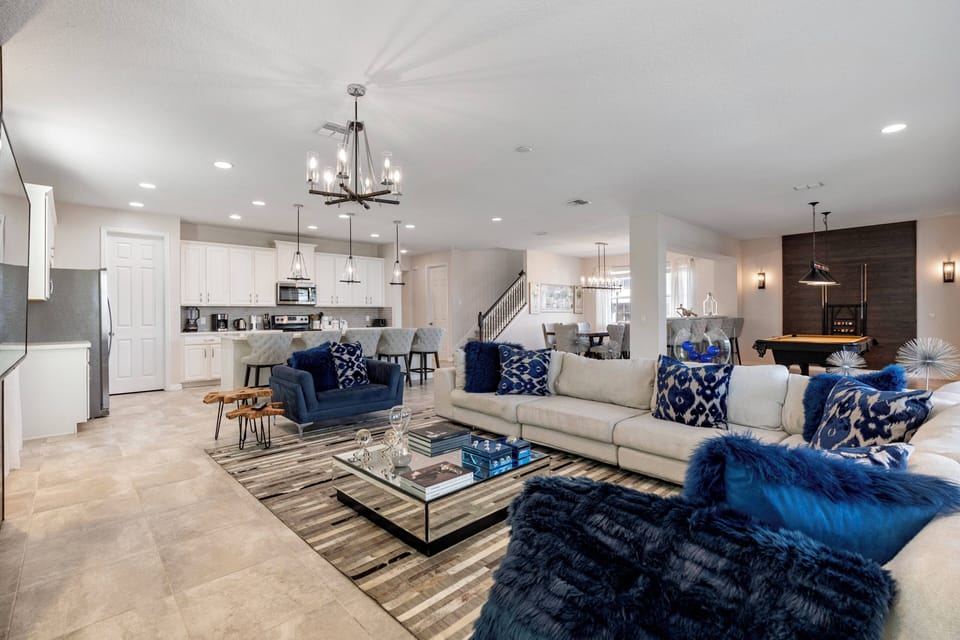 Enter a bright, spacious living area where plush navy accents beautifully contrast warm neutrals. The stylish sectional invites you to relax, and the elegant chandelier adds a sophisticated touch to the open layout.