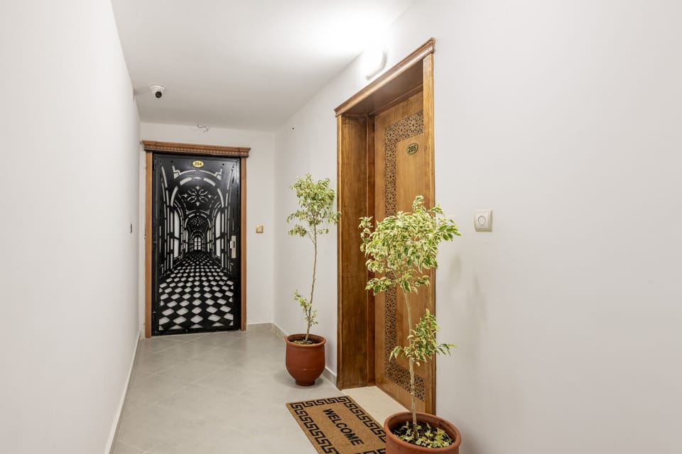 This inviting entrance welcomes you to the apartment. A warm welcome message sits above the wooden door, accented by lush potted plants creating a homey first impression.