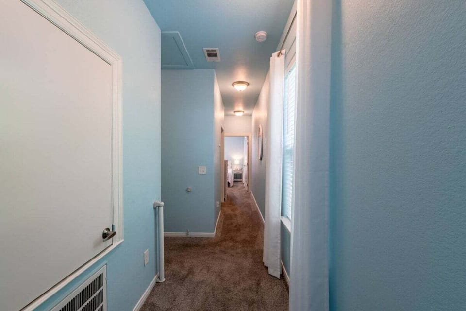 Long interior hallway with carpet flooring, coastal paint colors, and spacious layout connecting bedrooms and living spaces.