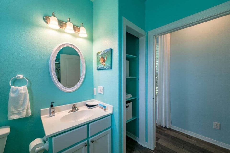 Modern bathroom vanity with round mirror, bright lighting, turquoise walls, and convenient layout perfect for vacation rental guests.