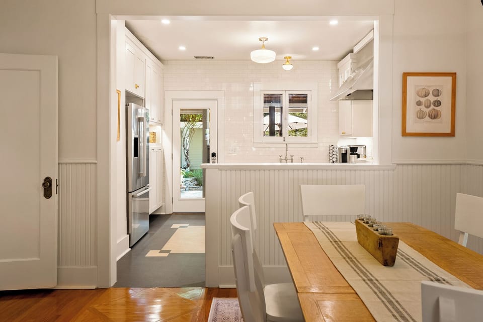 This charming home features a functional gourmet kitchen that seamlessly connects to the formal dining area, offering a sleek stainless steel refrigerator and custom white cabinetry with gold hardware.