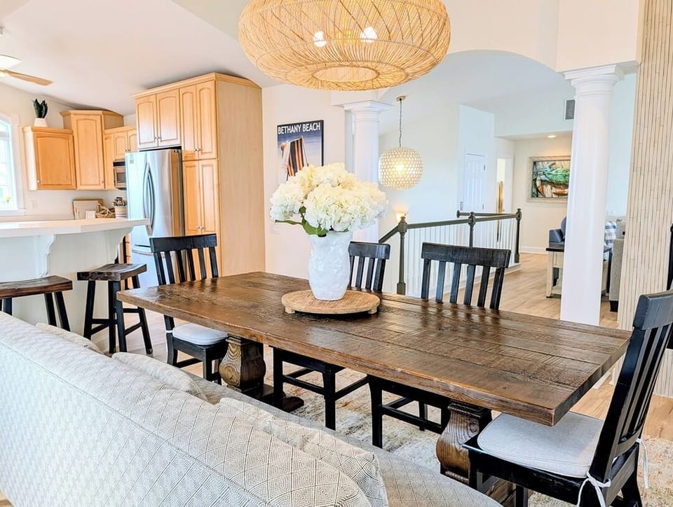 33 Inlet View North Bethany Beach Dining and Kitchen - A view of the dining area with a rustic wood table and seating, positioned adjacent to an open kitchen featuring light wood cabinetry.