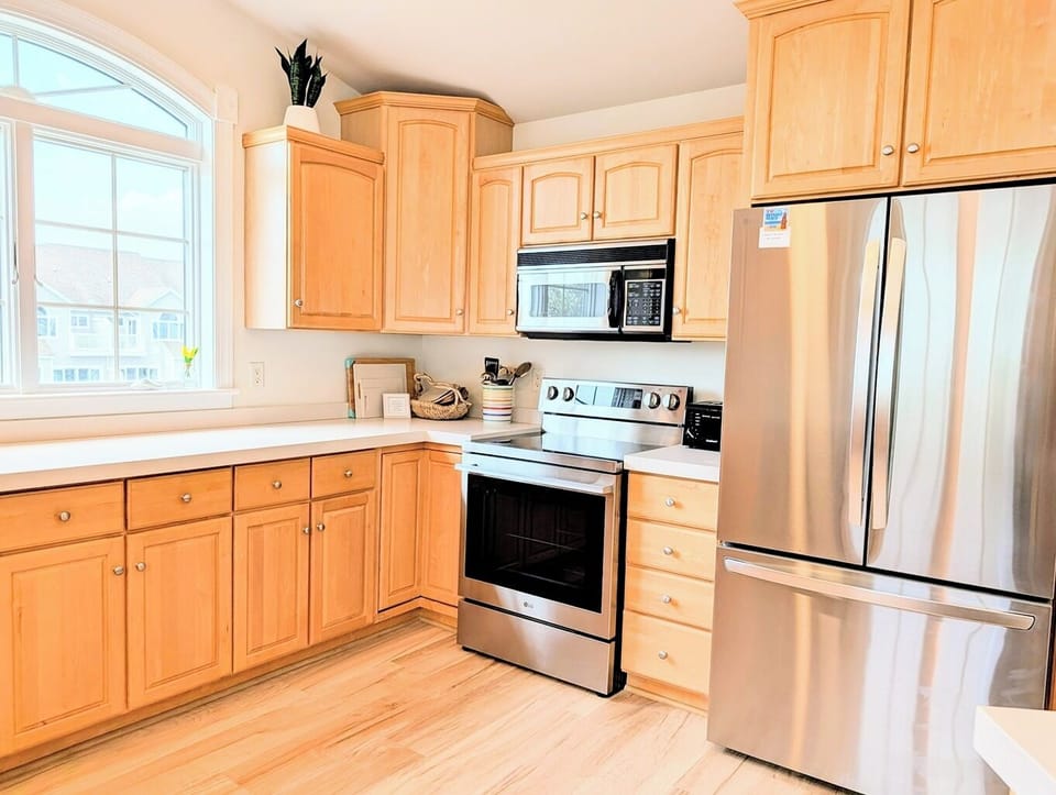 33 Inlet View North Bethany Beach Kitchen - A well-lit kitchen featuring light wood cabinetry, stainless steel appliances, and a window that brings in natural light.