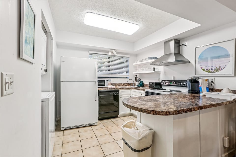 - Full kitchen with white appliances, oven, and range hood for easy meal prep
- Marble style counters offer generous workspace with plenty of storage space
- Bright window light keeps the kitchen airy and comfortable for cooking