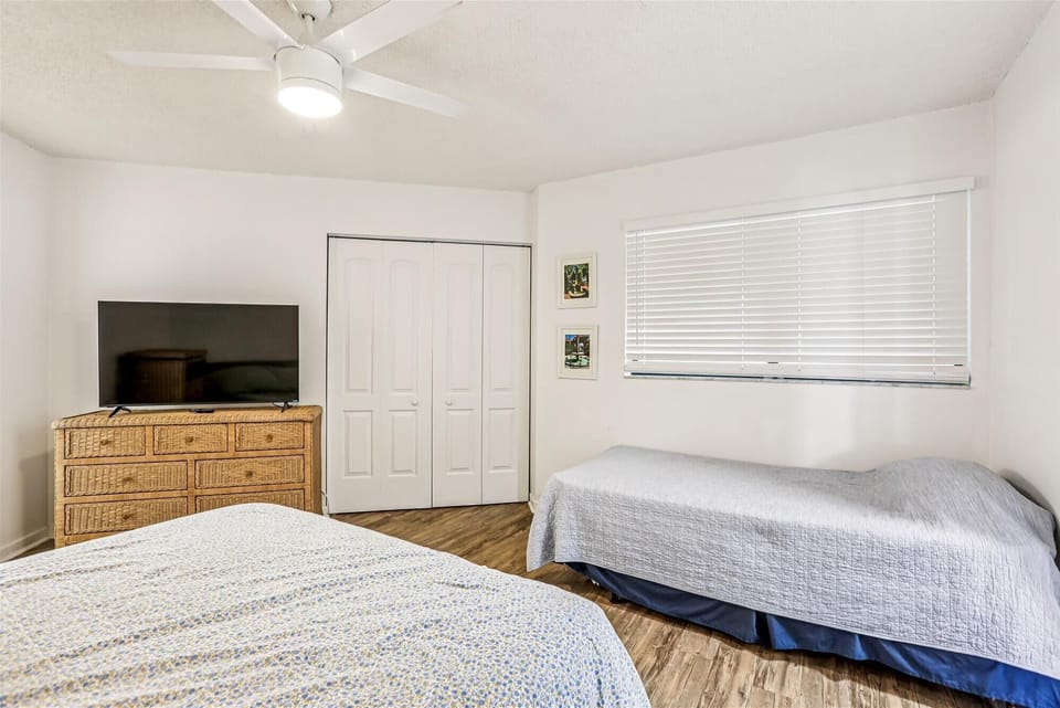 - Cozy guest room with queen bed and additional twin bed for flexible sleeping
- Flat-screen TV and rattan dresser provide entertainment and convenience
- Large window brings natural light while blinds offer added privacy