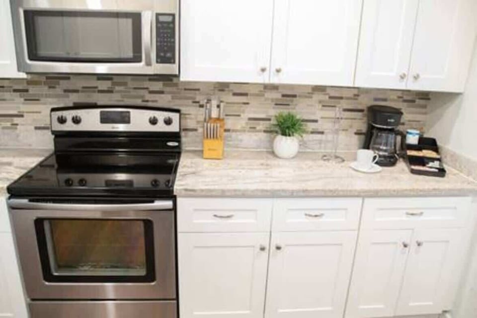 Fully equipped modern kitchen featuring stainless steel appliances, sleek white cabinetry, and a stylish tile backsplash. With plenty of counter space and all essential cookware provided, it's perfect for preparing delicious meals during your stay.
