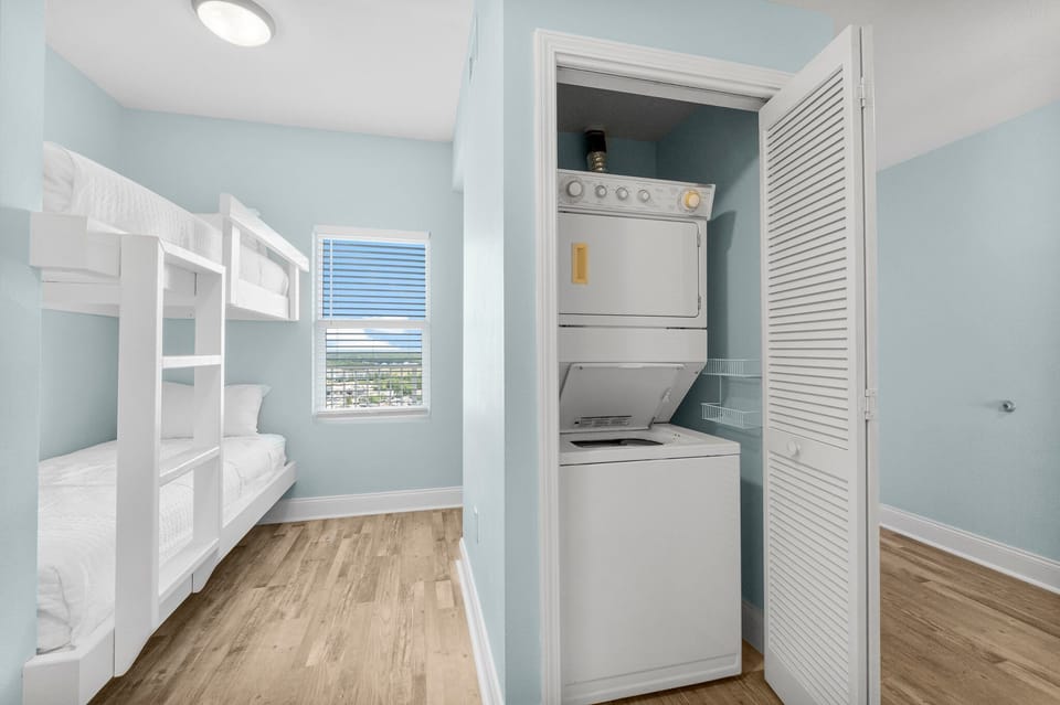 Laundry area with stacked washer and dryer next to a bunk bed room with natural light
