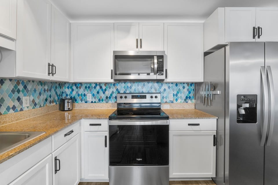 Modern kitchen featuring stainless steel appliances and a blue patterned tile backsplash.