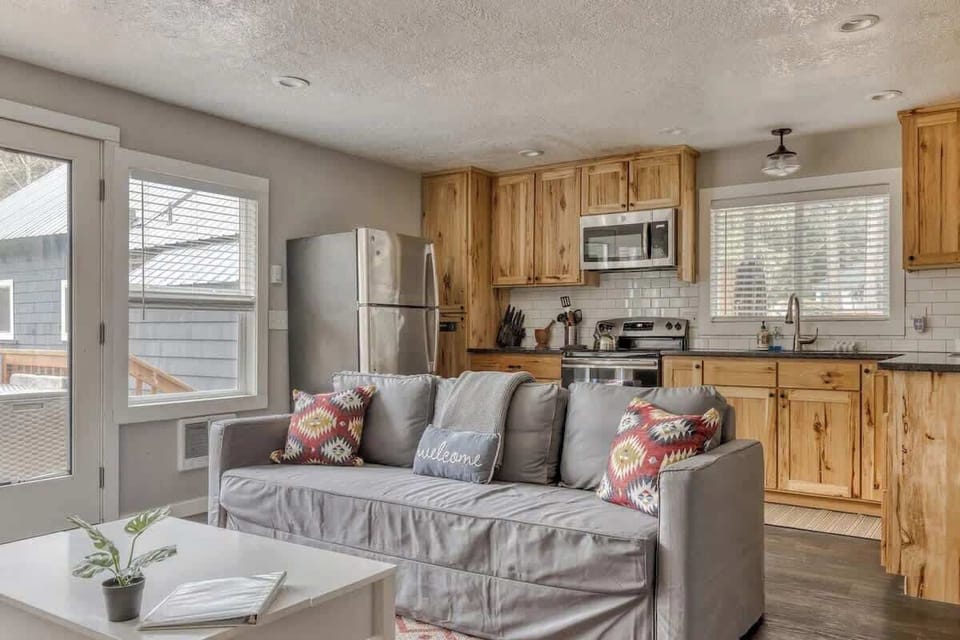 Bright, cozy cabin with natural wood cabinets, modern appliances, and a comfy gray sofa—perfect for relaxing after outdoor adventures.
