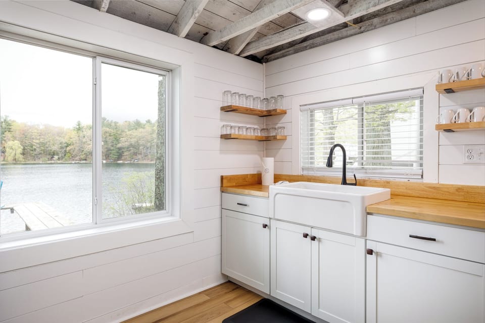 Sunny kitchen corner w/ farmhouse sink, open shelves & calming lake views.