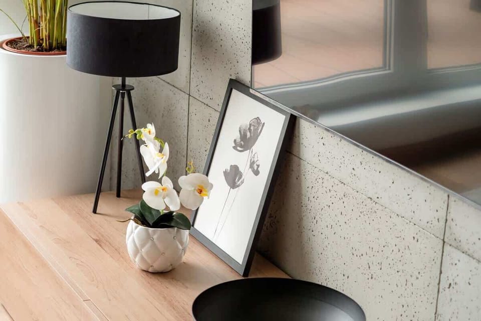 The stylish composition with a black tripod lamp, white orchids in a ceramic vase, and a black-and-white artwork creates an elegant decorative accent in the interior.