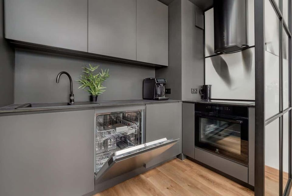 The modern kitchenette with gray cabinets, an open dishwasher, and a coffee machine on the countertop offers functionality in an elegant, compact design.