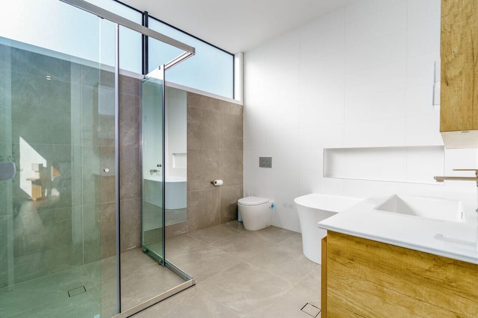 Indulge in luxury within this sleek and spacious bathroom, complete with a walk-in shower, modern fixtures, and a luxurious oversized bathtub. Appreciate the clean lines and abundant natural light in this impeccably designed space.