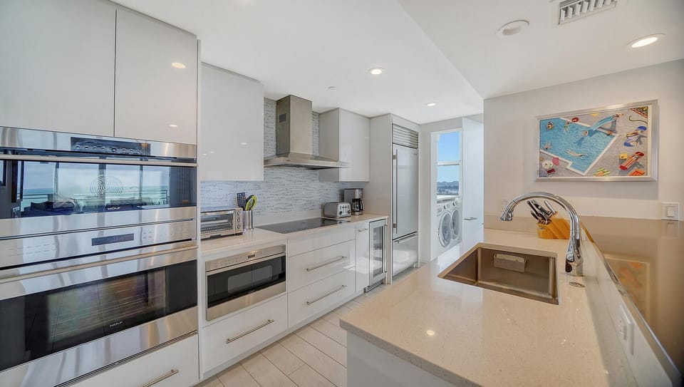 White quartz countertops extend along the kitchen with stainless steel appliances and a mosaic tile backsplash.