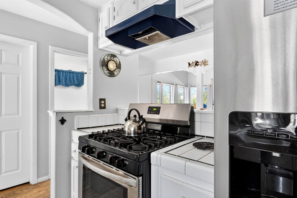 Bright white kitchen with tile counters, stainless steel appliances, and cheerful blue accents.