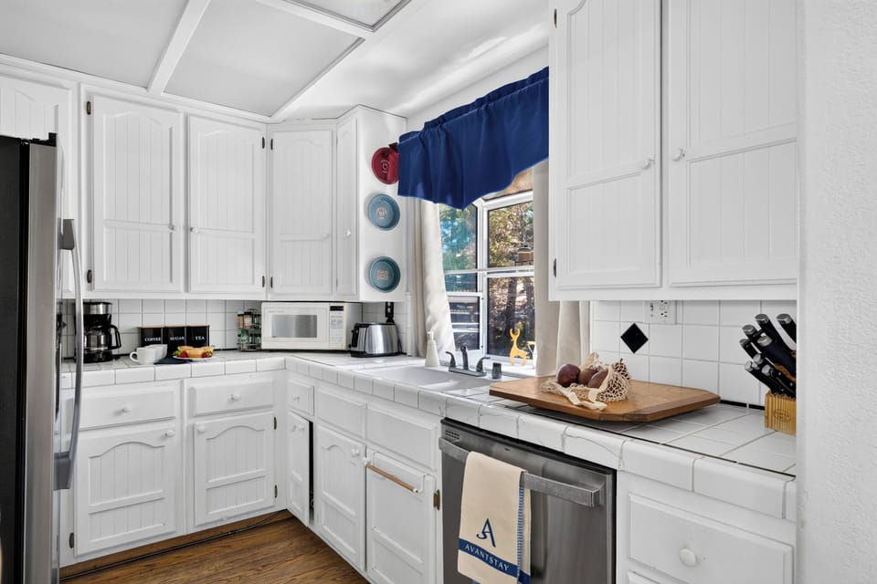 Bright white kitchen with tile counters, stainless steel appliances, and cheerful blue accents.
