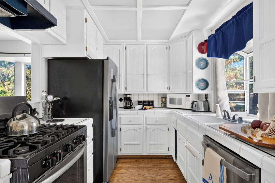Bright white kitchen with tile counters, stainless steel appliances, and cheerful blue accents.