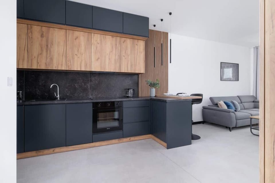 A well-designed kitchen and living area with matte black and wooden cabinetry, and a breakfast bar for dining.