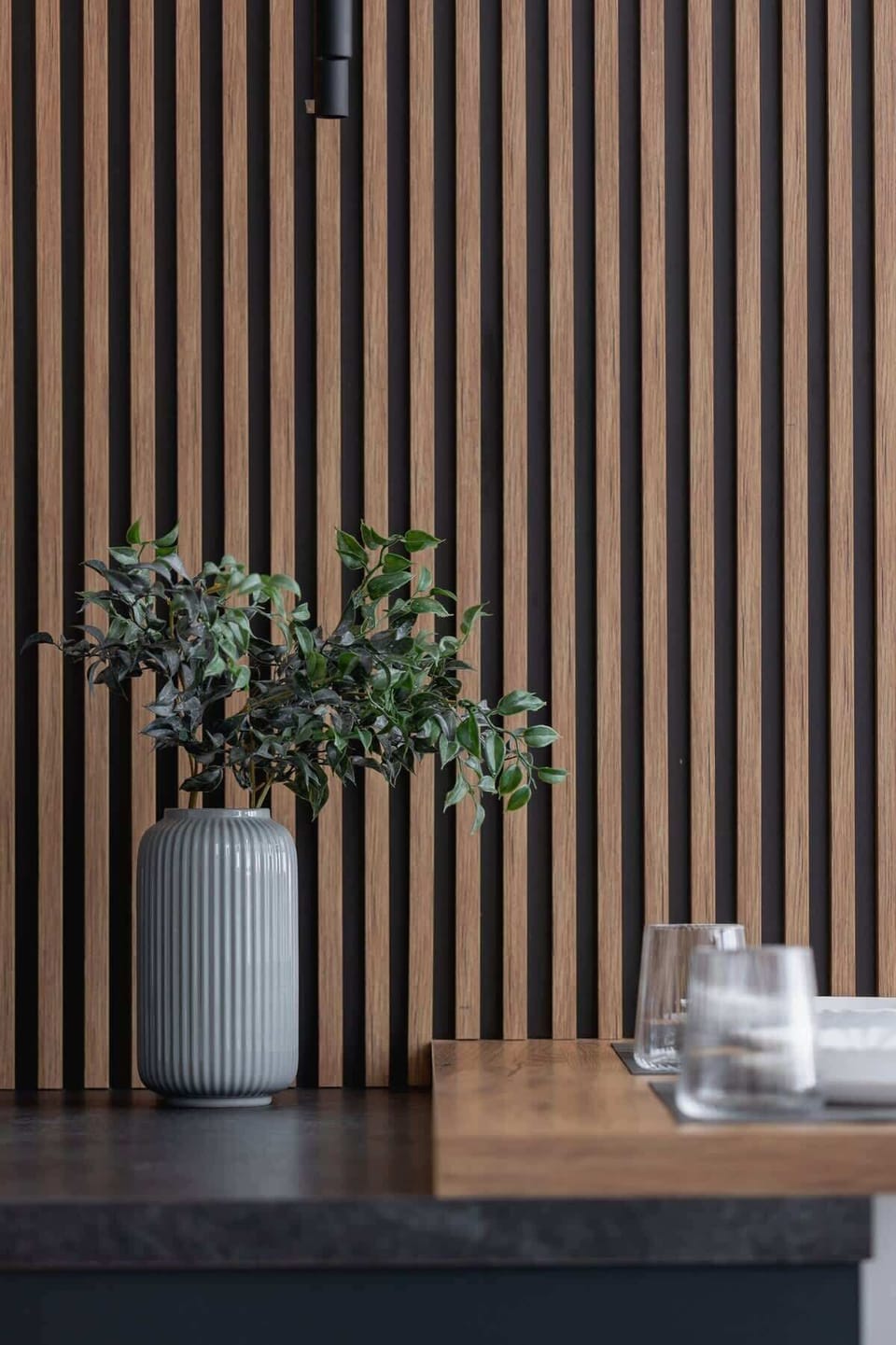 A section of a living room wall featuring vertical wooden slats, decorated with a small plant and candle.