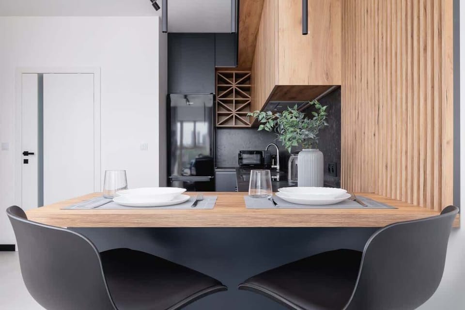 A dining area with a wooden table, modern chairs, and a kitchen in natural wood tones and gray accents.