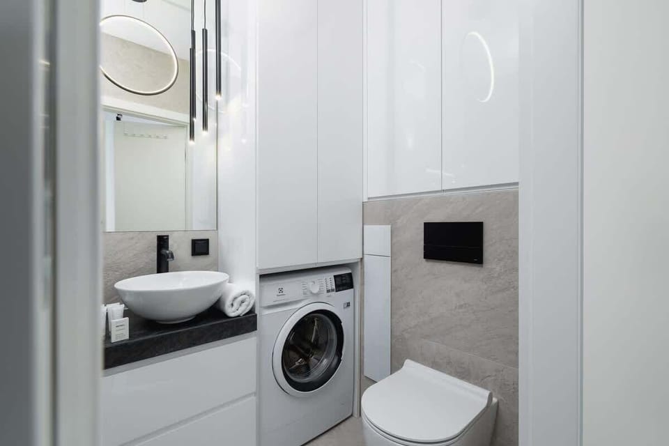 A bathroom with white and gray tiles, a washing machine, and minimal decor for a clean aesthetic.