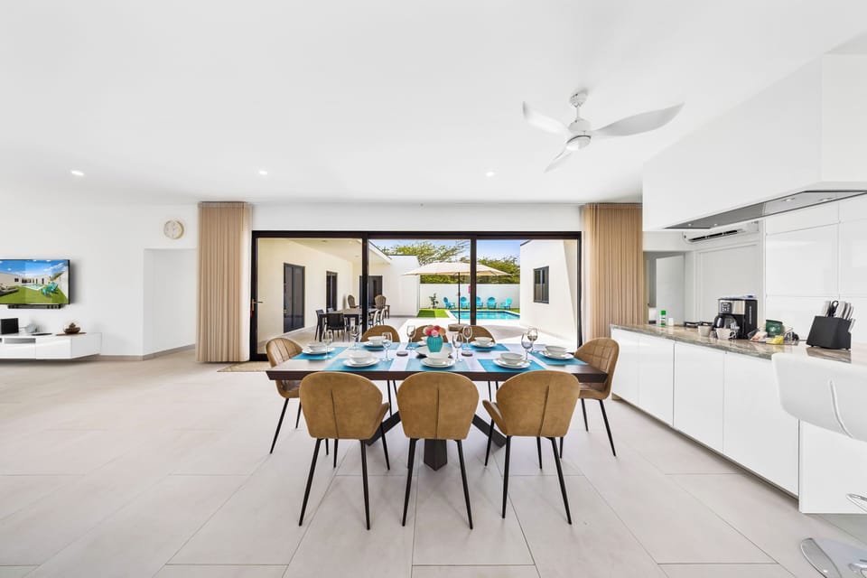 Thoughtfully organized dining area of the home in Noord, Aruba - Stunning 8 persons dining table in front of the open kitchen - Beautifully decorated space with lovely wall paintings - Big and bright doors leading to the backyard