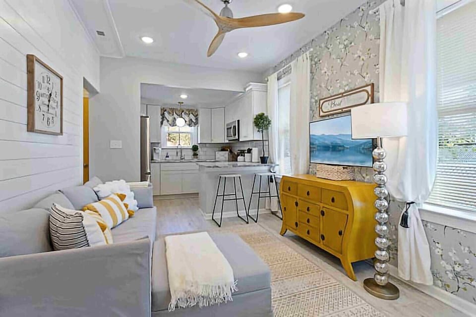 This versatile living room caters to all your needs.  Relax on the plush grey sofa and enjoy your favorite shows on the smart TV.  The spacious layout with carpeted flooring and layered rugs provides ample space for relaxation, entertaining, or simply hanging out. The convenient staircase connects you to the second floor, creating a well-connected living environment.  This styl...