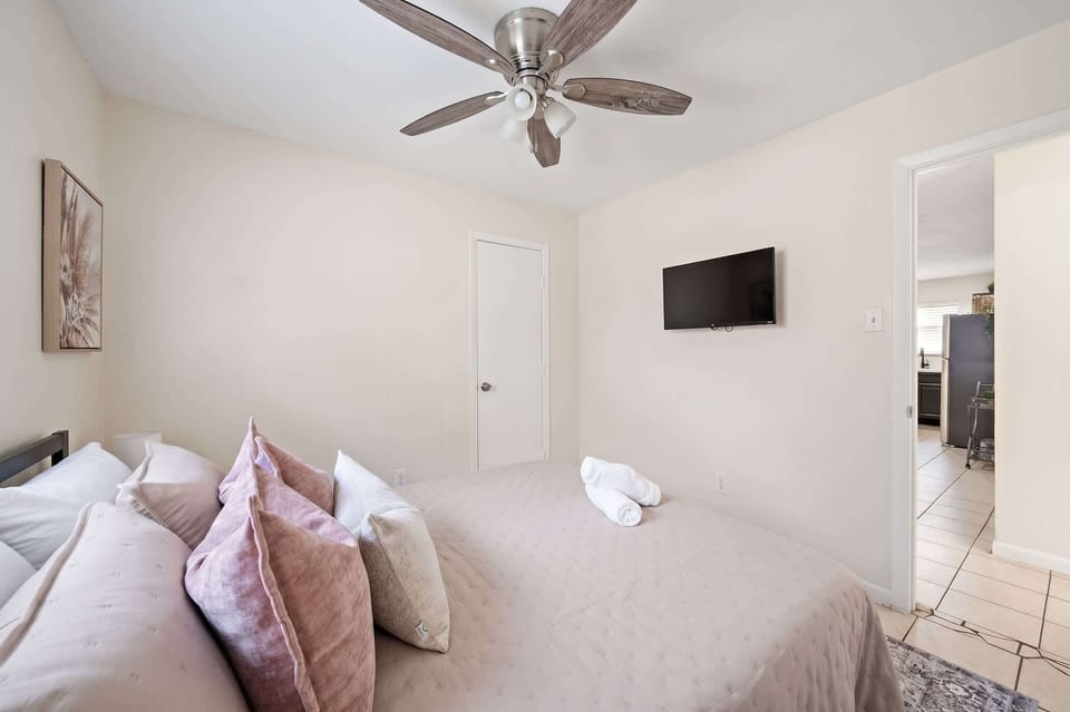 Bedroom: Clean lines and clever details. This modern bedroom features a wall-mounted TV, stylish ceiling fan, and a view into the bright kitchen.