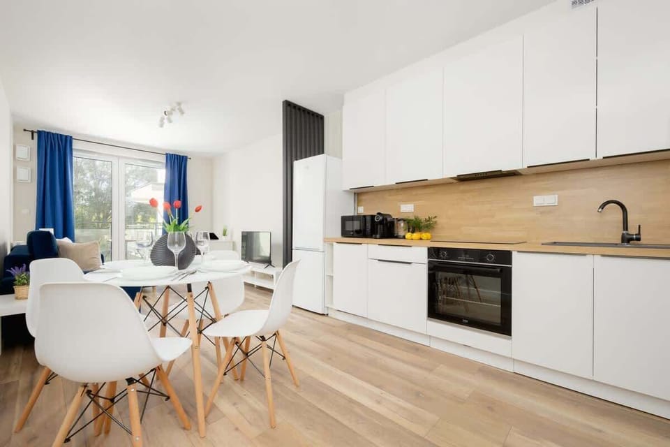 A modern open-concept kitchen and dining area with white cabinetry, a built-in oven, and a round table with two chairs, creating a clean and functional space.