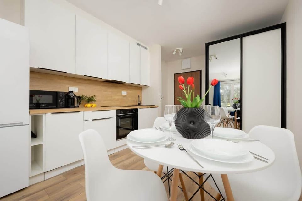 A modern open-concept kitchen and dining area with white cabinetry, a built-in oven, and a round table with two chairs, creating a clean and functional space.