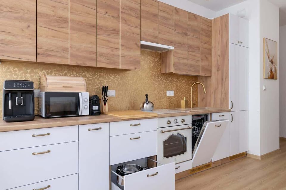 A sleek kitchen with light wood cabinetry, white countertops, and modern built-in appliances.

