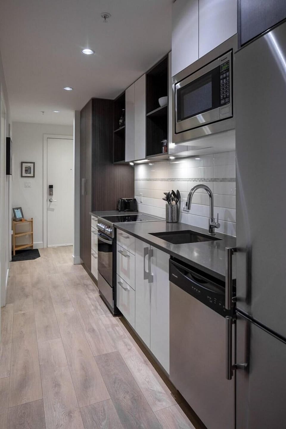 Efficient kitchen corridor layout featuring dark cabinetry, solid surface counters, and integrated dishwasher.
