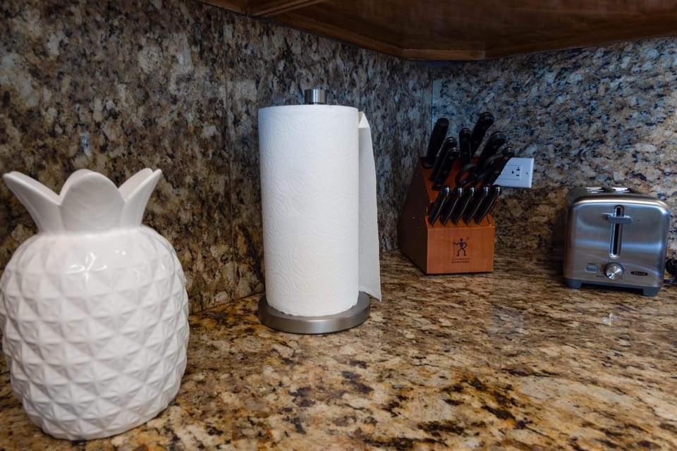 A beautifully decorated kitchen with a granite countertop, stainless steel toaster, and a tropical pineapple accent, perfect for a beachside retreat.