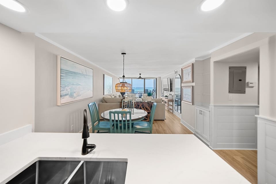Your open-concept kitchen flows seamlessly into the bright living space, where coastal artwork and ocean views create a serene retreat.