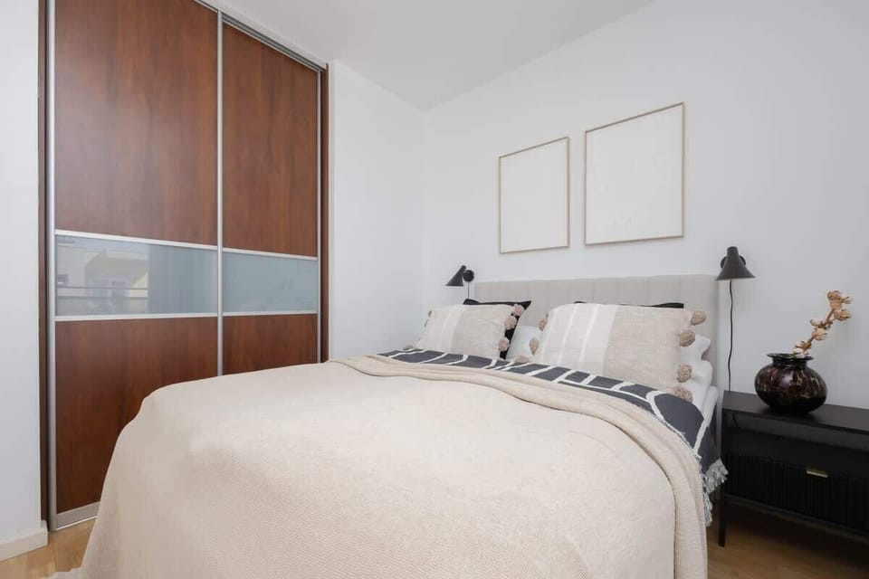 A bedroom with a dark wooden wardrobe, bright curtains, and a soft beige bedspread.

