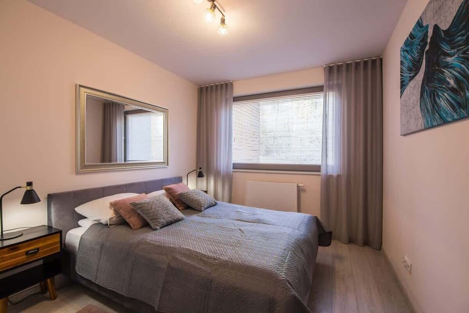 A softly lit bedroom with a large bed, taupe curtains, and a neutral color palette that invites rest.

