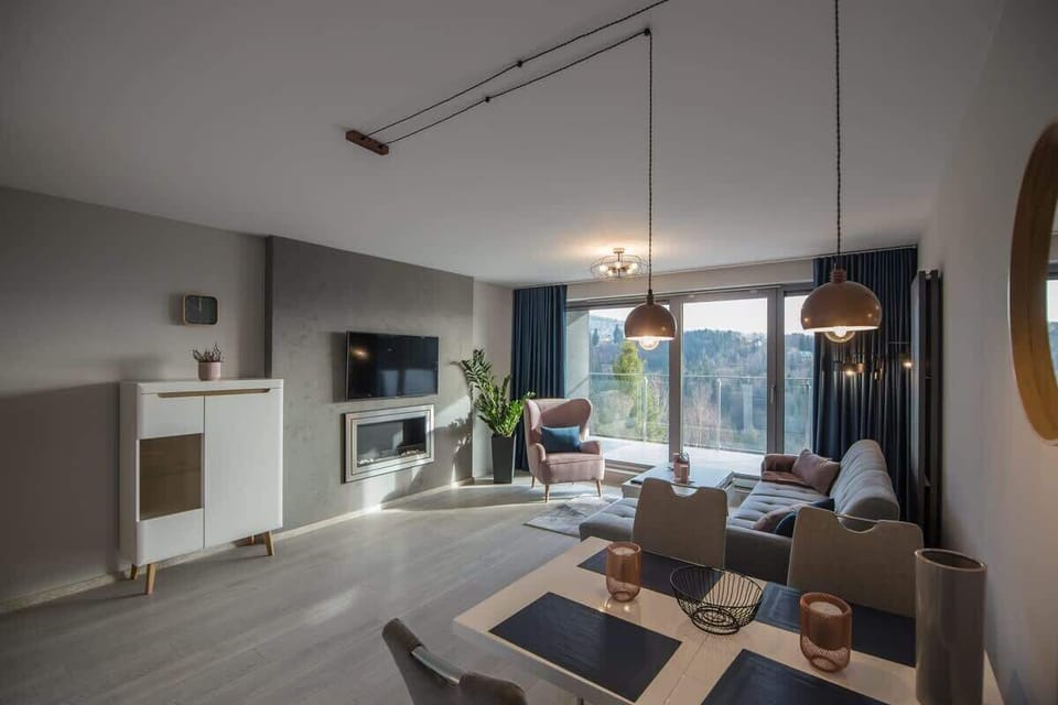 A contemporary open-plan living room with soft lighting, L-shaped sofa, and a dining table set for four.

