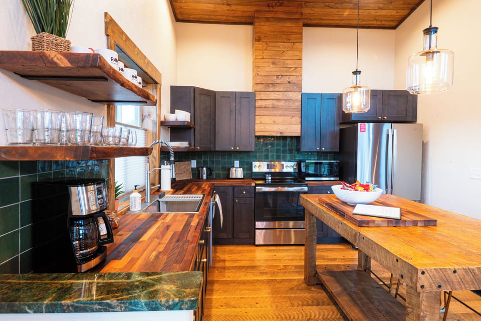 A second kitchen angle shows the open shelving, range, dishwasher, walnut butcher-block counters, and warm custom woodwork.