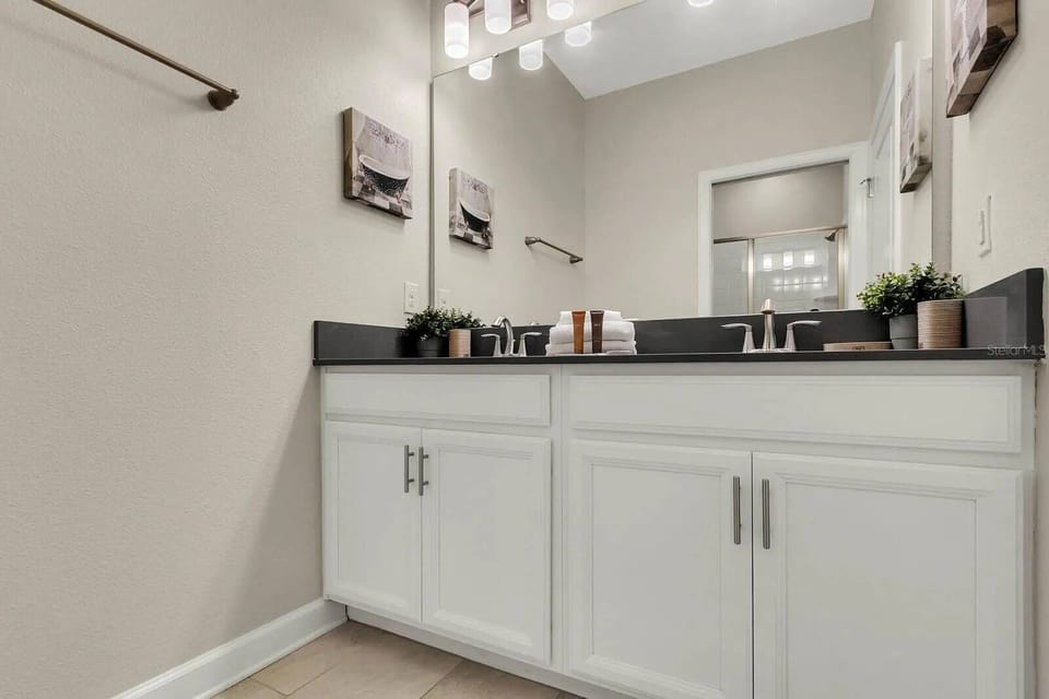 Experience this chic bathroom with a sleek black countertop and bright white cabinetry, blending style and function. Thoughtful decor enhances the modern vibe, ensuring a refreshing atmosphere for your stay.