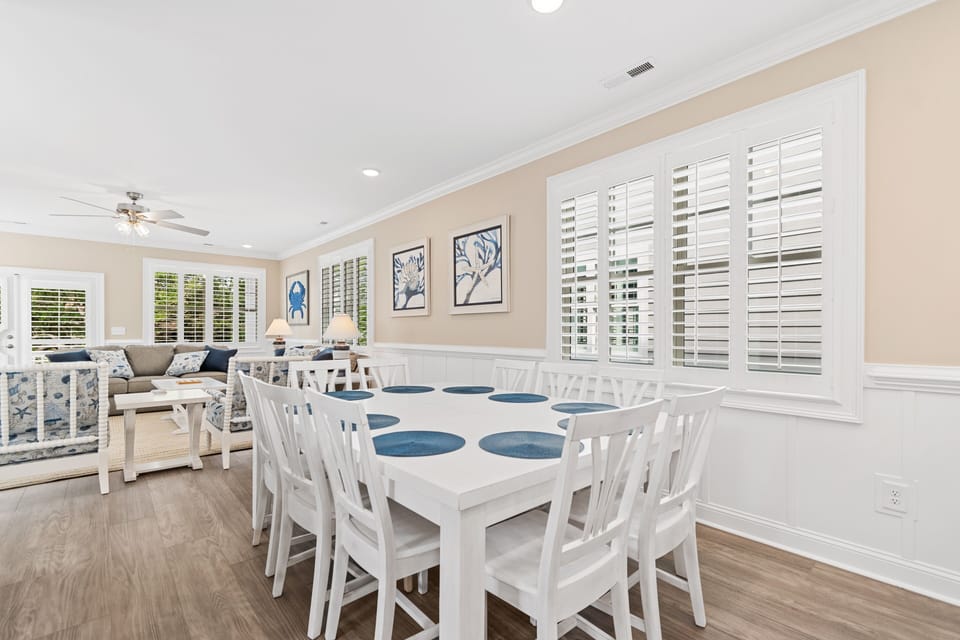 Your elegant dining space flows seamlessly into the living area, with white plantation shutters filtering natural light over the spacious table for eight.