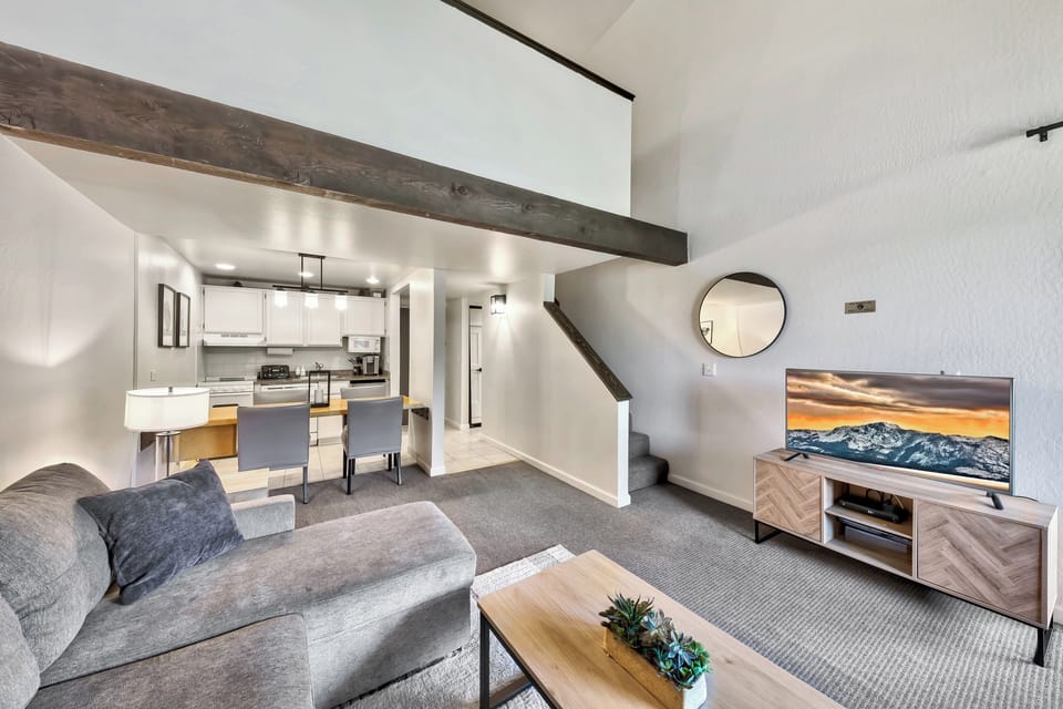 Relax in your spacious living area where rustic beams meet modern style, complete with a cozy sofa and open kitchen.