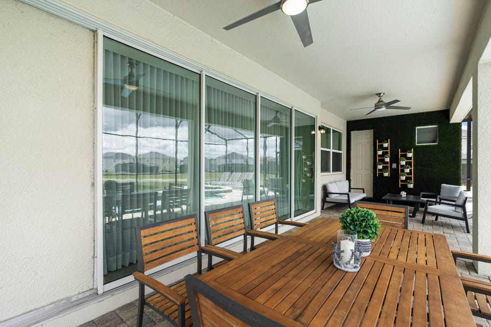 Step onto the spacious covered patio featuring a rustic wooden dining table, perfect for al fresco meals. With sleek ceiling fans and lush greenery, it's an ideal spot for relaxing or entertaining by the pool.