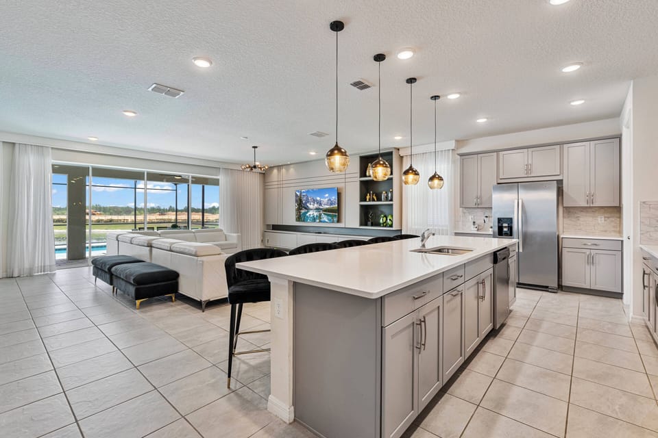 Welcome to a stylish kitchen with sleek gray cabinetry and a spacious white quartz island, perfect for meal prep or morning coffee. The open layout invites natural light and offers lovely views of the outdoor area.