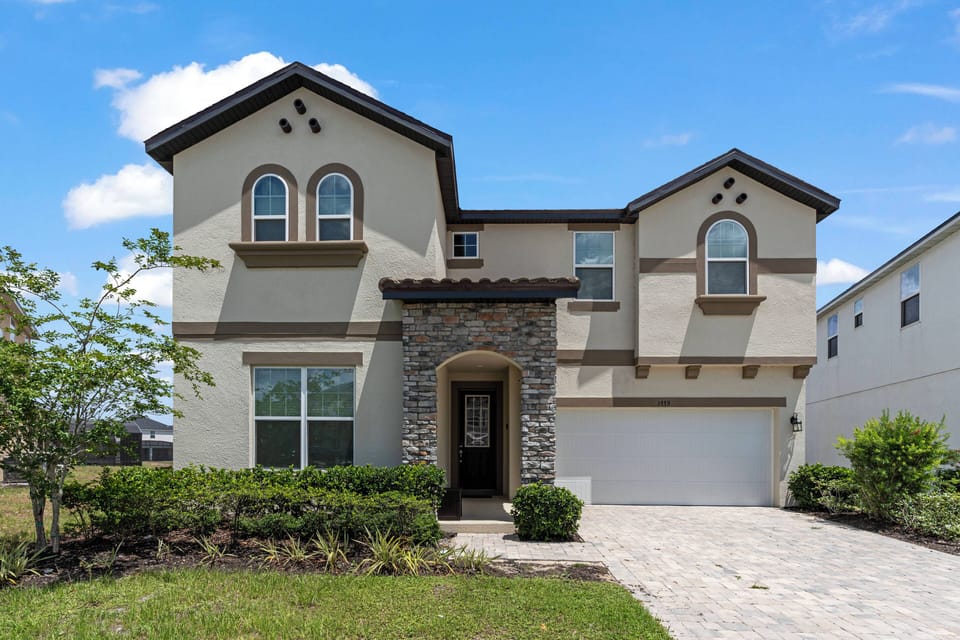 This charming vacation home features a stunning stone facade and unique architectural details, creating a warm first impression. The bright blue sky and landscaped yard enhance its inviting curb appeal for a delightful stay.