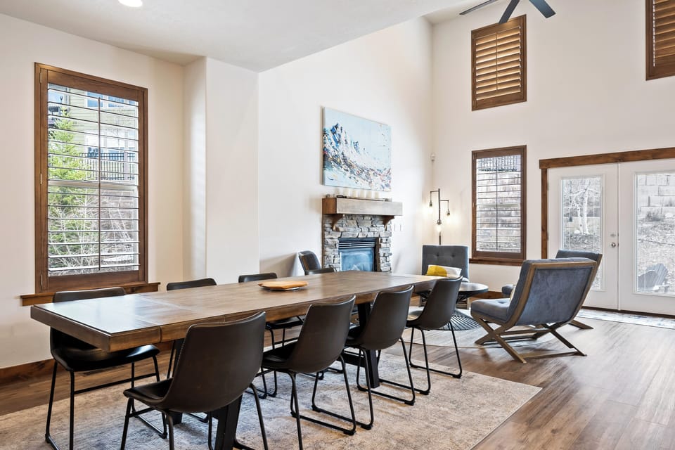 - Dining room with large wooden table and seating  
- Fireplace adds warmth and cozy charm to the room  
- Bright windows and open design for group meals