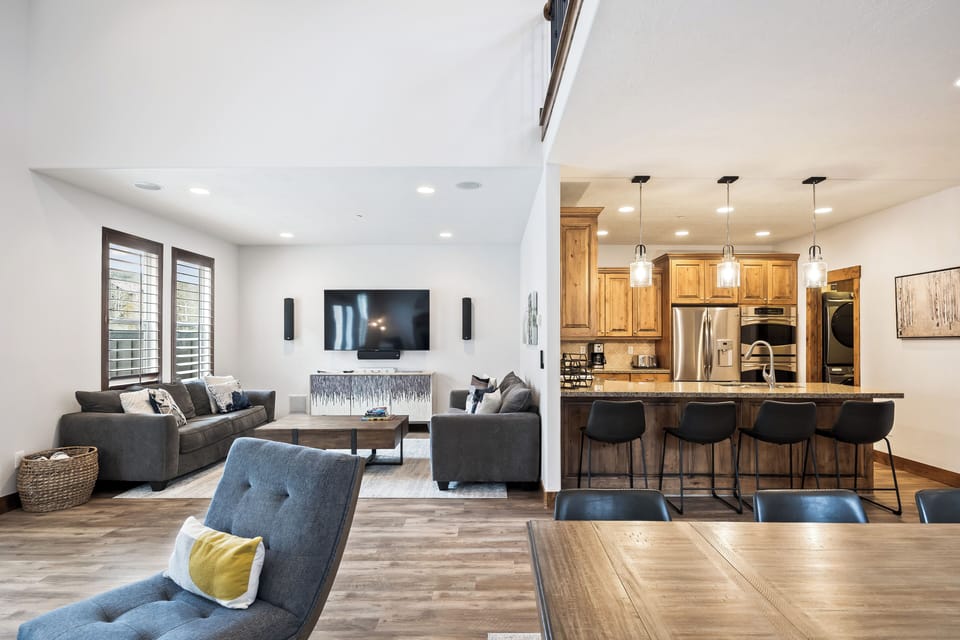 - Spacious living room with flat screen TV and sofas  
- Open kitchen and breakfast bar in the background  
- Modern layout designed for comfort and convenience