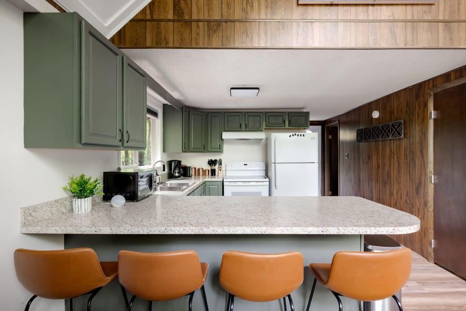 Modern kitchen with green cabinetry and a spacious breakfast bar with leather stools.