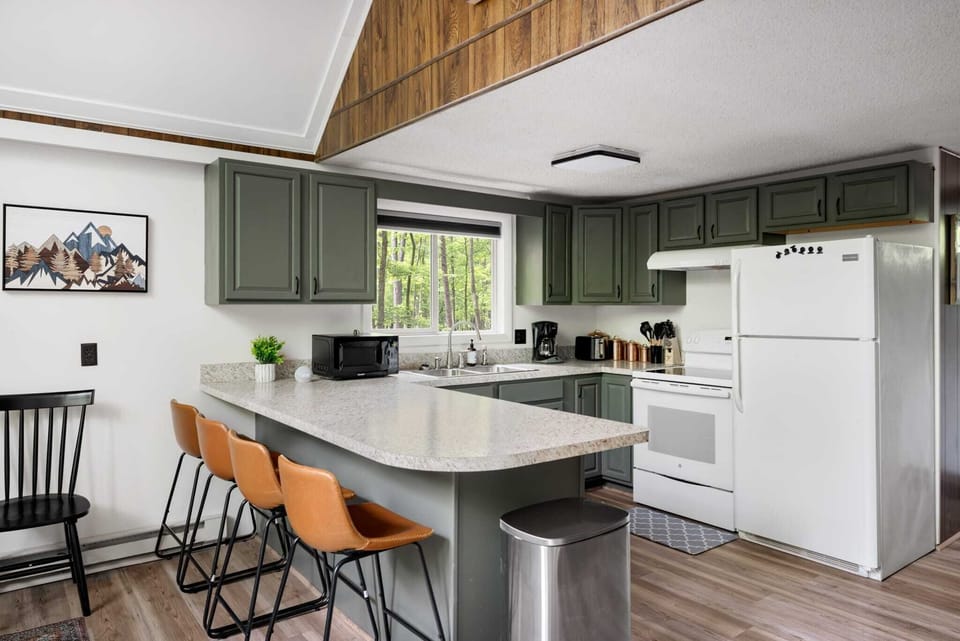 Modern kitchen with green cabinetry and a breakfast bar overlooking a wooded view.